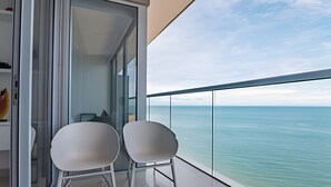 Ein Balkon mit zwei weißen Stühlen, einer Glastür und Blick auf das Meer.