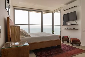 Ein modernes Schlafzimmer mit großem Fenster, einem Bett, einem an der Wand montierten Fernseher und einem kleinen Regal mit Dekoration.
