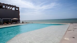 A swimming pool with a view of the ocean, lounge chairs, and umbrellas. - Spectacular 1 Bedroom Apt - 14th Floor Morros City (Cartagena)