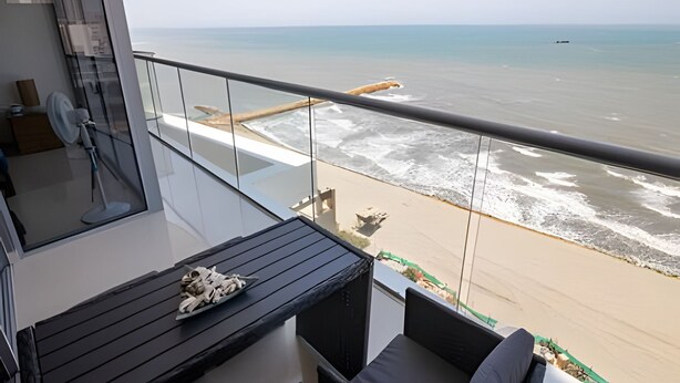 A balcony with a view of the beach, a table with a plate of food, and a chair. - Spectacular 1 Bedroom Apt - 14th Floor Morros City (Cartagena)