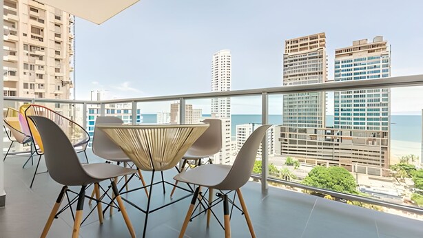Un balcon avec une table et des chaises, offrant une vue sur le paysage urbain et la mer.