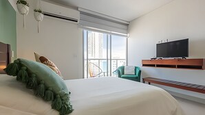 Une chambre d’hôtel moderne dotée d’un grand lit, d’un téléviseur fixé au mur et d’un balcon offrant une vue sur la ville.