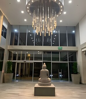 Ein moderner Gebäudeeingang mit großer Glasfassade, einer zentralen Skulptur und einer runden Leuchte darüber.
