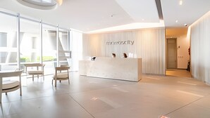 En moderne reception med et minimalistisk design, med receptionsdisk, siddeområde og store vinduer der lukker naturligt lys ind.