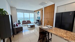 Cozinha moderna com área de refeições, grandes janelas com vista para a cidade e sala de estar com sofá e cadeiras.