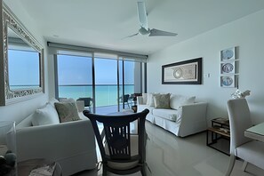 A spacious living room with a large window, a ceiling fan, and a dining area with a table and chairs. - Luxurious 2-bd Apt on the 20th Floor - Morros City (Cartagena)