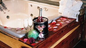 A bathtub with a bottle of champagne, two glasses, rose petals, and a green rose. - Green Briar Cabin a beautiful private log cabin (Marietta)