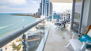 Ein Balkon mit Blick auf das Meer und die Stadtlandschaft, ausgestattet mit Liegestühlen und einem Glasgeländer.