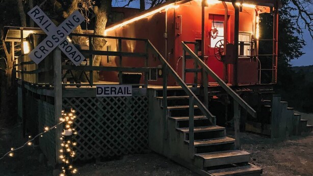 Un pequeño edificio rojo con una escalera que sube a una puerta, ubicado al lado de una señal de paso de tren.