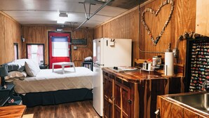 Una habitación pequeña y acogedora, con paneles de madera, una cama, una mesita, un refrigerador y un lavabo.
