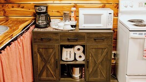 A kitchenette with a coffee maker, microwave, and stove. There are cabinets with drawers and a shelf with a kettle and cups.