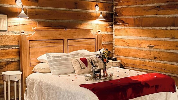 A cozy log cabin bedroom with a wooden headboard, a bedside table, and two wall-mounted lamps.