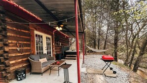 A rustic cabin with a covered porch, a sofa, a table, and a barbecue grill.