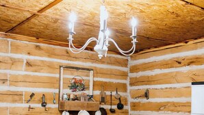 A rustic wooden room with a wooden table, two chairs, a chandelier, and kitchen utensils hanging on the wall.