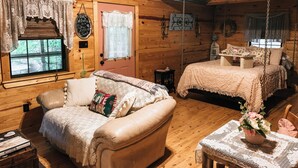 Une cabane chaleureuse avec un intérieur en bois, un canapé, un lit avec une balançoire suspendue et une petite table sur laquelle est posé un vase de fleurs.