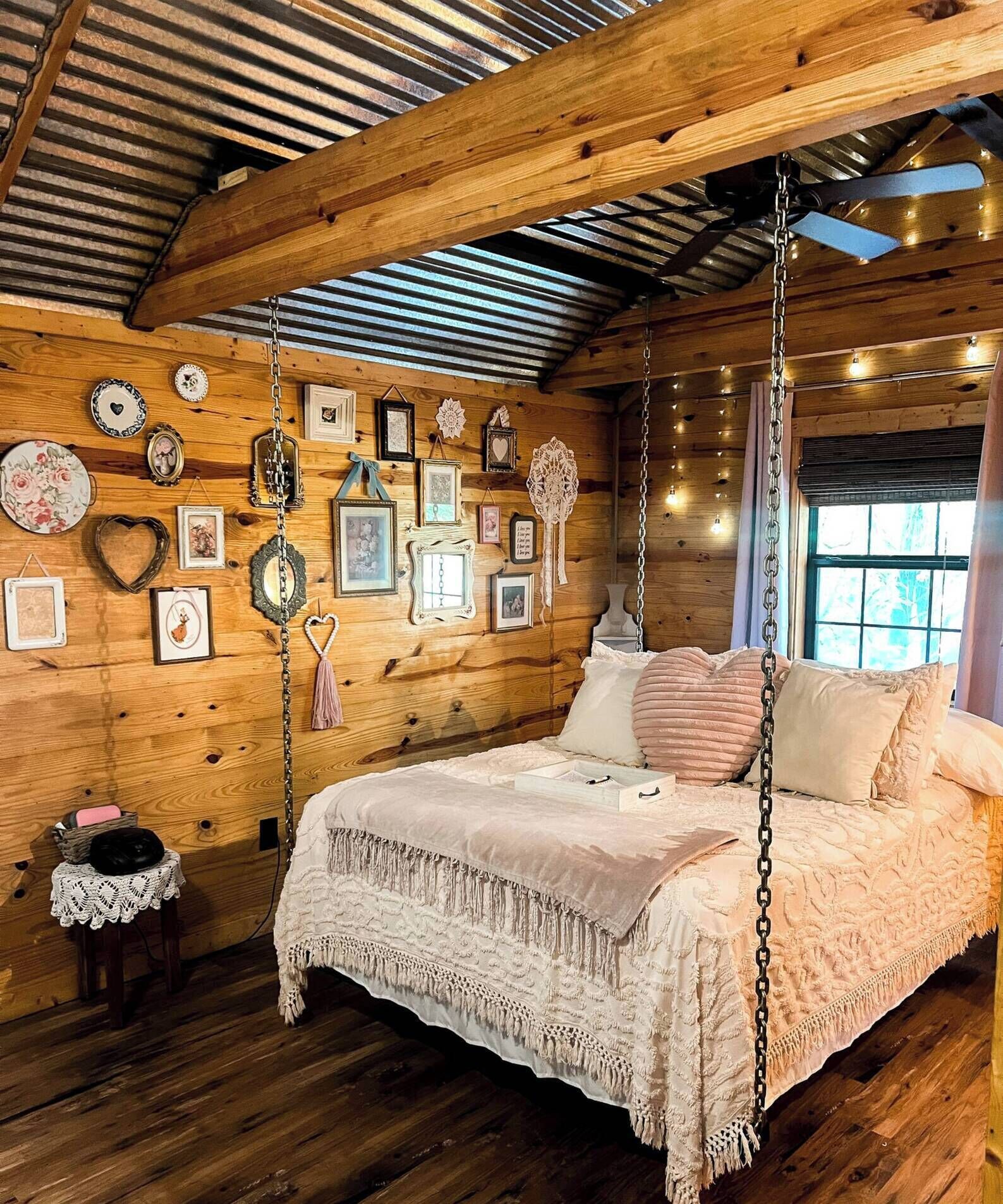 Un dormitori d'una cabana de fusta acollidora, amb llit, decoracions penjants i un sostre rústic.