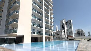 En modern byggnad med en swimmingpool, flera balkonger och en klar himmel.