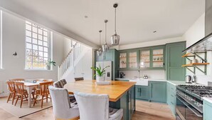 A spacious kitchen with a central island, wooden chairs, and a staircase leading to an upper level. - Stylish Stay w/ All you Need- The Old Grammar School (Kibworth)