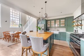 A spacious kitchen with a central island, wooden chairs, and a staircase leading to an upper level.