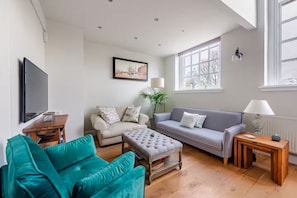 Ein Wohnzimmer mit einer Couch, einem Sessel, einem Hocker und einem Fernseher.