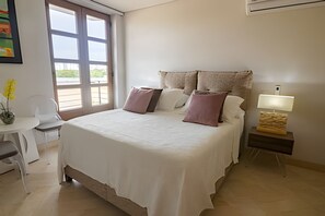 A bedroom with a large bed, a bedside table with a lamp, a chair, and a window with a view of greenery. - Spectacular view of San Felipe Castle! (Cartagena)