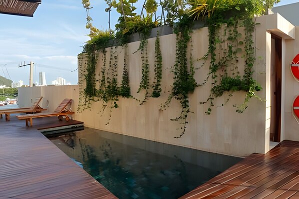 A rooftop pool with wooden loungers and a concrete wall covered in green vines. - Spectacular view of San Felipe Castle! (Cartagena)