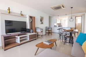 A modern living room with a flat-screen TV, a wooden entertainment unit, a sofa, a coffee table, and a dining area with chairs and a table. - Beautiful 2 Bedroom Apt on the 11th Floor-Morros City (Cartagena)
