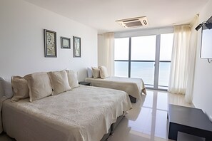 A hotel room with two beds, a desk, and a large window offering a view of the sea. - Beautiful 2 Bedroom Apt on the 11th Floor-Morros City (Cartagena)