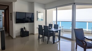 A modern living room with a flat-screen TV, a dining table with chairs, and a balcony with a view of the sea. - Spectacular Ocean View - Infinito Building 1802 (Cartagena)