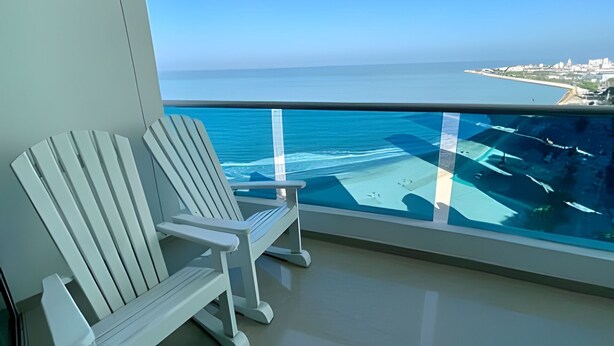 A balcony with a white chair, offering a view of the ocean and a distant shoreline. - Spectacular Ocean View - Infinito Building 1802 (Cartagena)