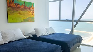 A hotel room with two beds, a large window with a view of the sea, and a painting on the wall. - Spectacular Ocean View - Infinito Building 1802 (Cartagena)