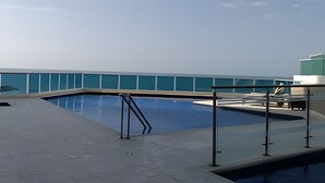 A swimming pool with a glass barrier, a metal ladder, and a view of the ocean. - Spectacular Ocean View - Infinito Building 1802 (Cartagena)