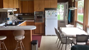 A kitchen with wooden cabinets, a stainless steel refrigerator, a stove, and a dining area with a table and chairs.