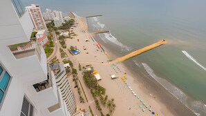 A beach with a long wooden pier extending into the sea, surrounded by buildings and a clear sky. - Luxurious 3 Bedroom apt - 3303 Palmetto Beach (Cartagena)