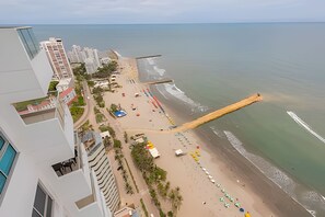 A beach with a long wooden pier extending into the sea, surrounded by buildings and a clear sky. - Luxurious 3 Bedroom apt - 3303 Palmetto Beach (Cartagena)