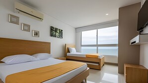 A modern hotel room with a large bed, a smaller bed, a bedside table, a wardrobe, and a large window offering a view of the sea. - Luxurious 3 Bedroom apt - 3303 Palmetto Beach (Cartagena)