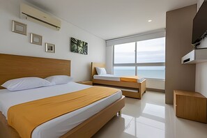 A modern hotel room with a large bed, a smaller bed, a bedside table, a wardrobe, and a large window offering a view of the sea. - Luxurious 3 Bedroom apt - 3303 Palmetto Beach (Cartagena)