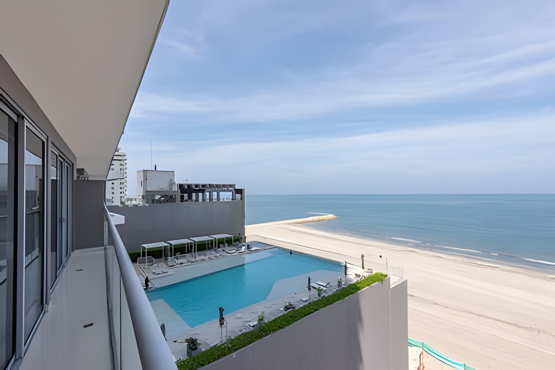 En modern hotellbalkong med en pool som vetter ut mot en strand.