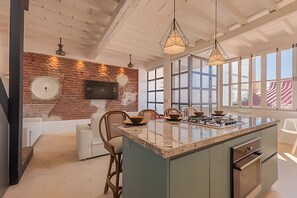 Une cuisine moderne dotée d’un grand îlot central, d’un mur en briques au style rustique et de grandes fenêtres.