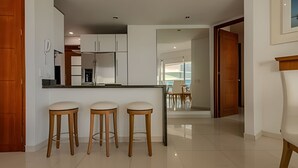 A modern kitchen with white cabinets, a central island with stools, and a dining area visible through an open door. - Spectacular Ocean View - Ed. Infinito 2302 (Cartagena)