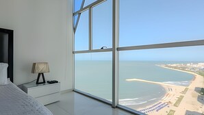 A bedroom with a large window overlooking a beach and cityscape. - Spectacular Ocean View - Ed. Infinito 2302 (Cartagena)