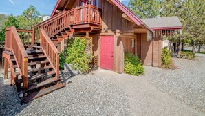 Une cabane en bois avec une porte rouge, un balcon et une allée gravillonnée.