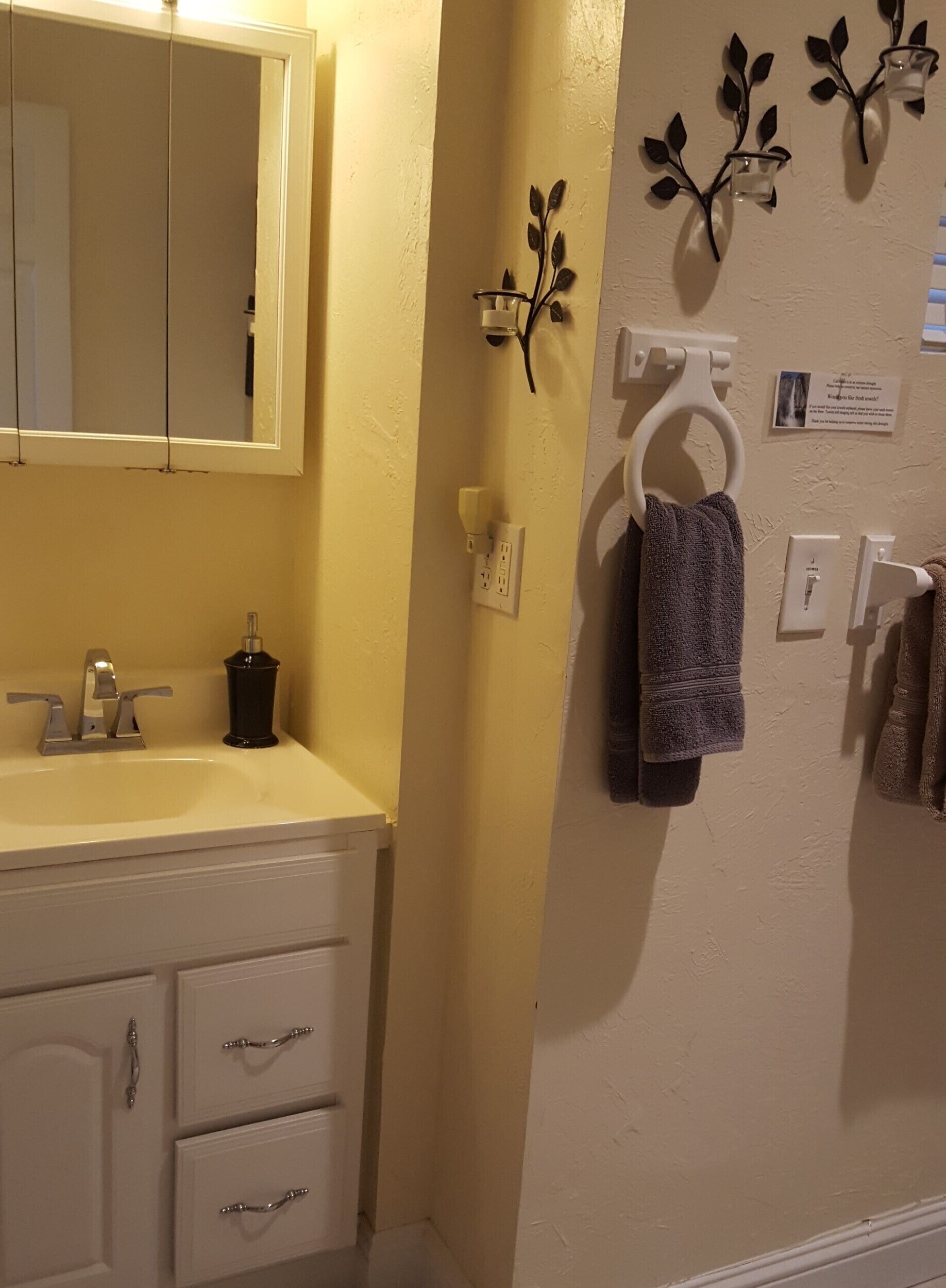 Ein Badezimmer mit Waschbecken, Spiegel, Handtuchhalter und einer Wandleuchte.