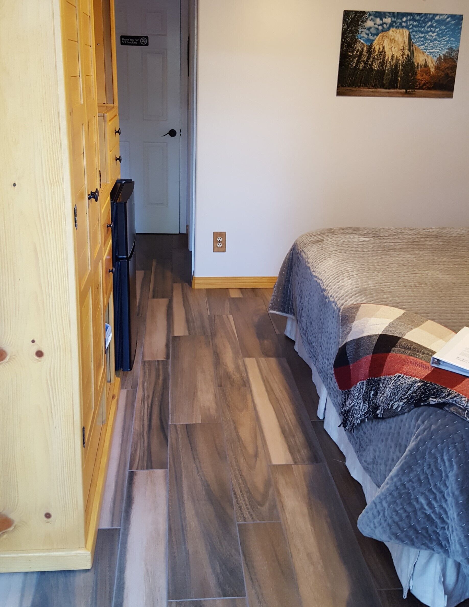 A bedroom with a bed, a wooden wardrobe, and a door with a sign.