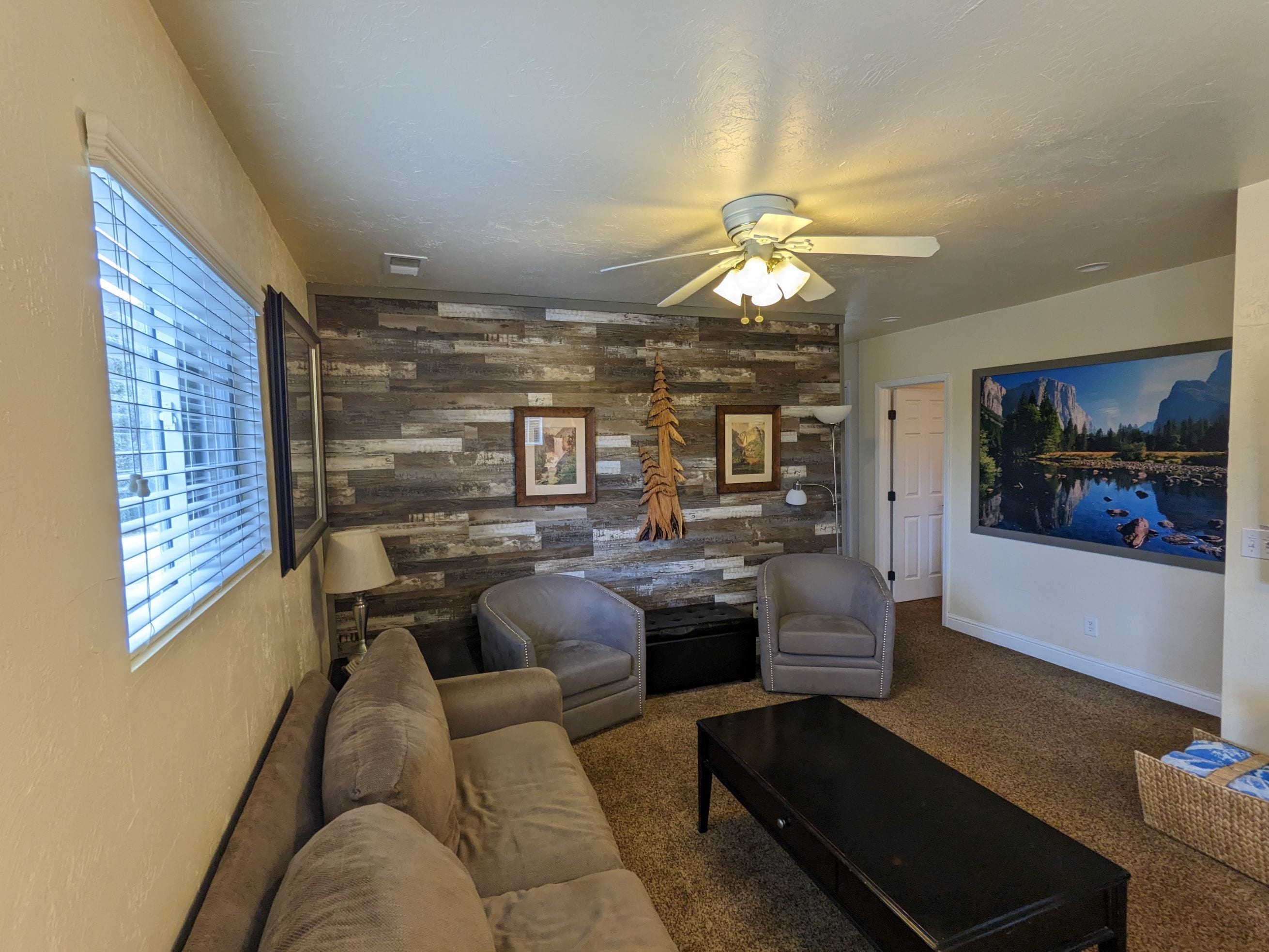 A living room with a sofa, chairs, a coffee table, a ceiling fan, a fireplace, and a large painting on the wall.