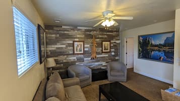 A living room with a sofa, chairs, a coffee table, a ceiling fan, a fireplace, and a large painting on the wall.