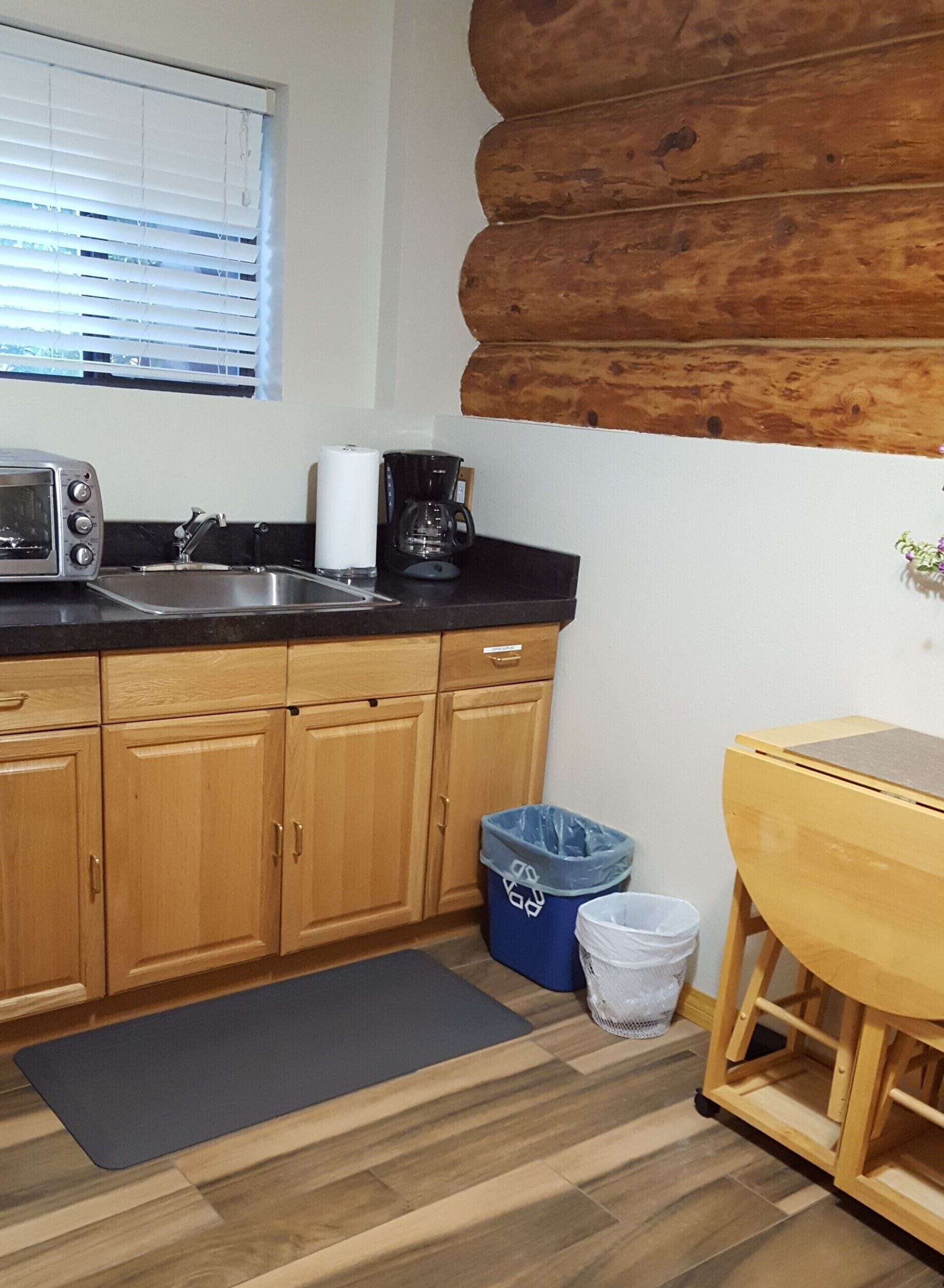Une cuisine compacte avec des meubles en bois, un plan de travail noir, un grille-pain, une machine à café et une poubelle.