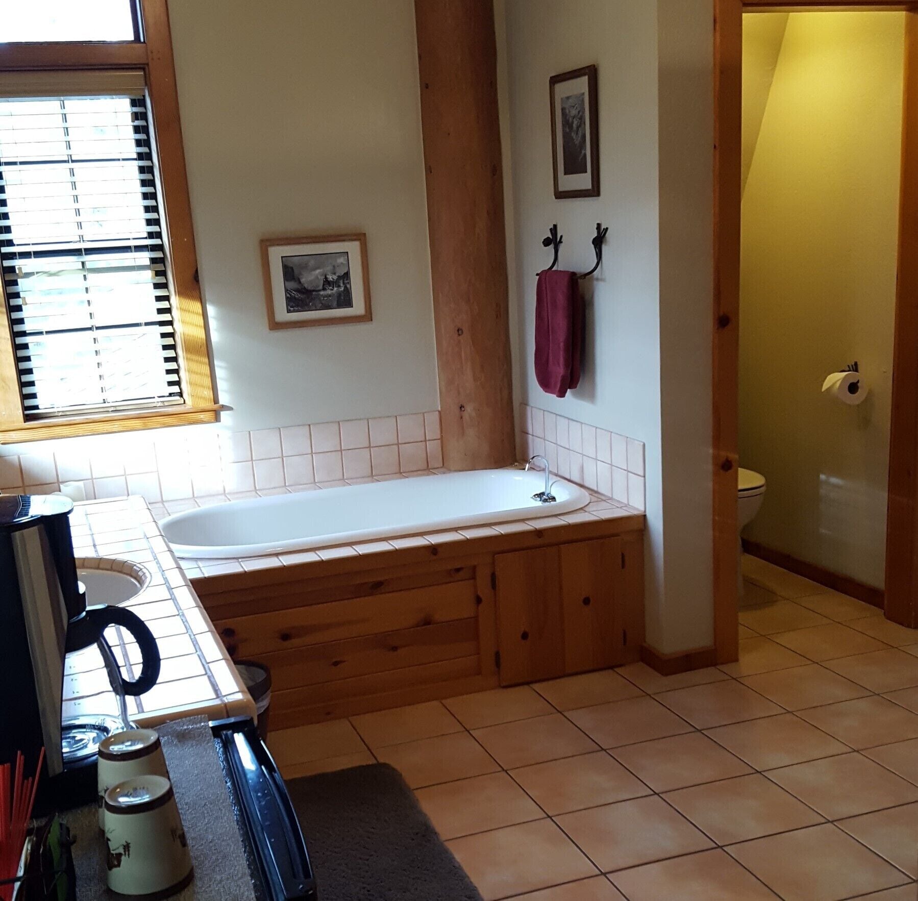Une salle de bain avec un meuble-lavabo en bois, une baignoire, des toilettes et une fenêtre avec des stores.