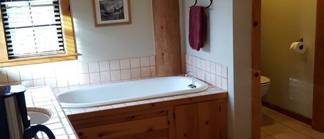 Une salle de bain avec un meuble-lavabo en bois, une baignoire, des toilettes et une fenêtre avec des stores.