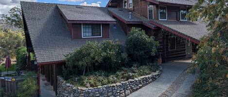 A log cabin with a stone retaining wall, a covered porch, and a view of the surrounding landscape.